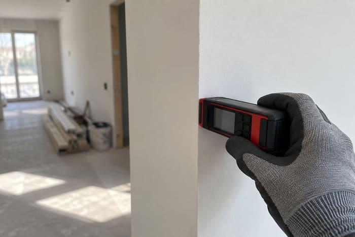 Инженер проводит контрольные замеры отклонений стены лазерным дальномером при приёмке отделки